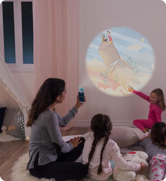 A few young girls point at a projected Moonlite image on the wall that mom is holding up