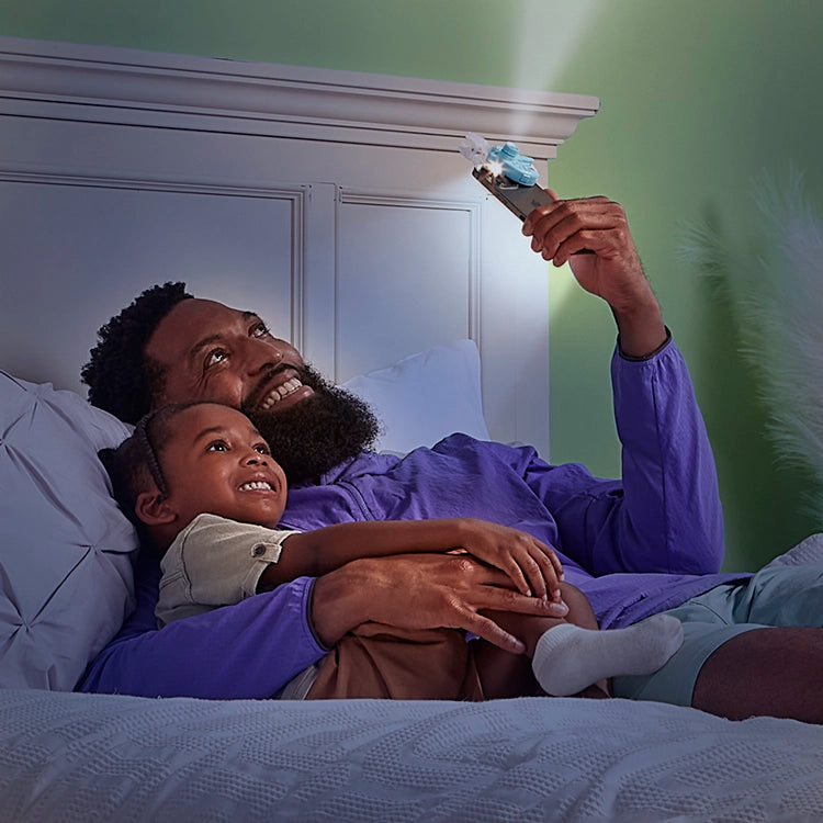 Man and child lying in bed reading with the Moonlite Projector.