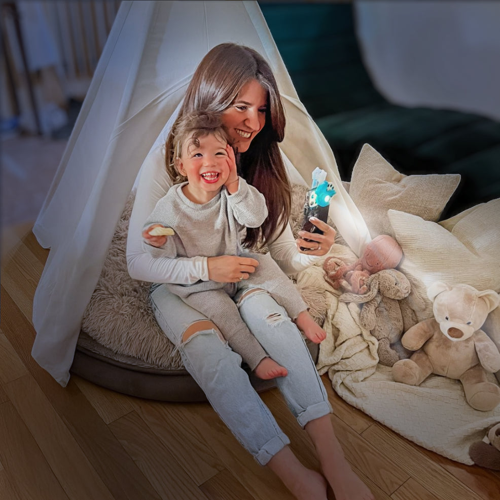 Woman and child sitting inside a small tent  reading with the Moonlite Storytime Projector