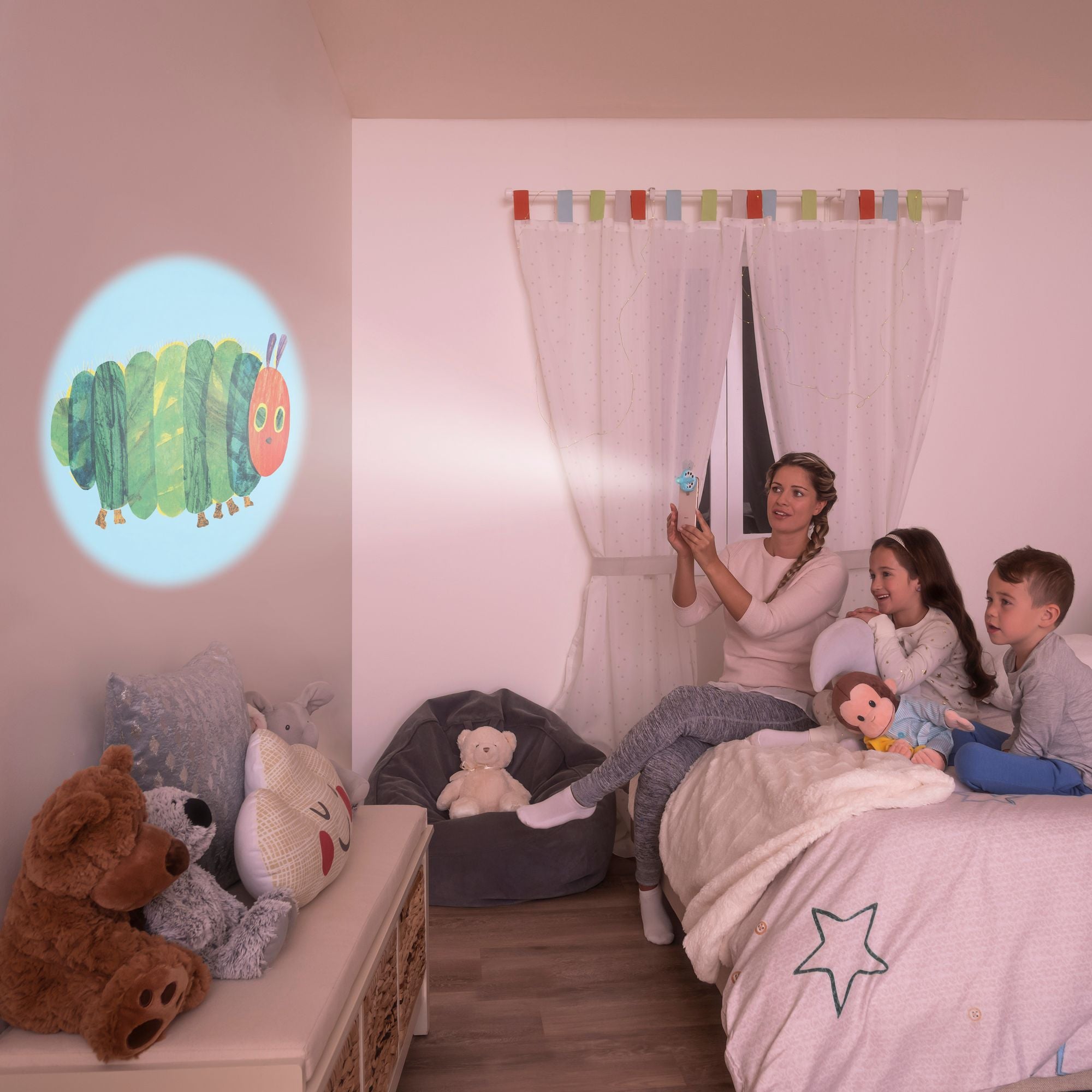 Mom with 2 Kids Projecting a Caterpillar Story by the bedroom wall